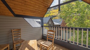 Een houten terras met een tafel en stoelen, uitzicht op bomen en gebouwen, en een balkonhek.