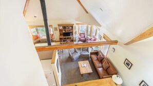Een woonruimte in loftstijl met een hoge plafond, zichtbare balken, een open haard en een gezellige zithoek.