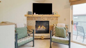 A living room with a fireplace, two chairs, and a television mounted above the fireplace.
