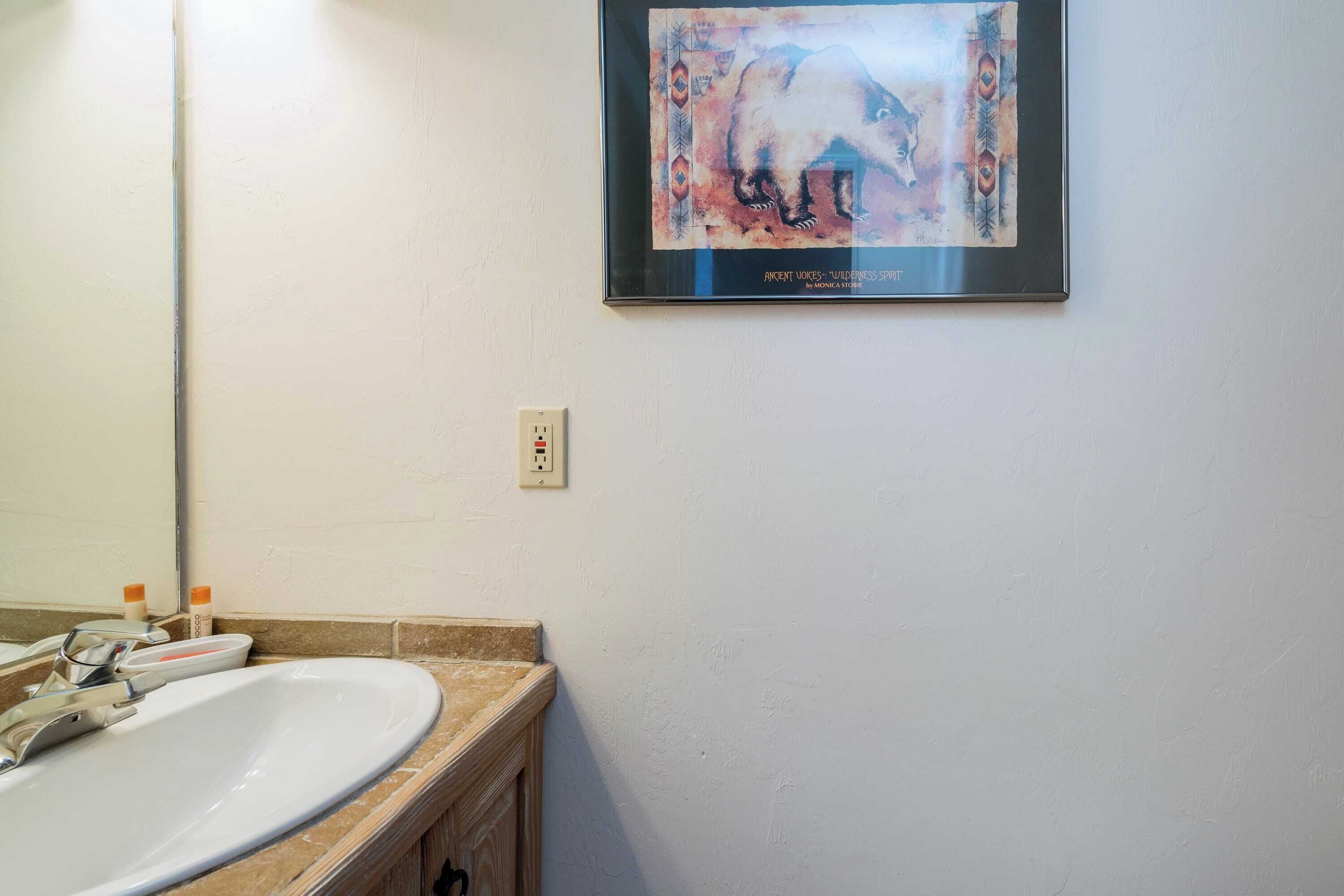 Un baño con un lavamanos blanco, un espejo y un cuadro en la pared.