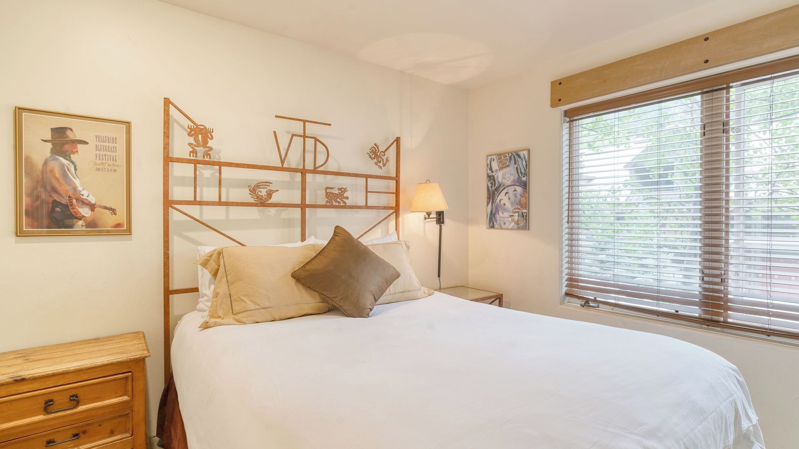 Un dormitorio con cama, mesita de noche, lámpara, ventana con persianas y decoración en la pared.
