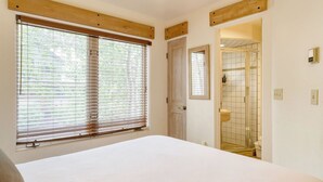 A bedroom with a large window, a door leading to a bathroom, and a bed.
