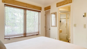 A bedroom with a large window, a door leading to a bathroom, and a bed.