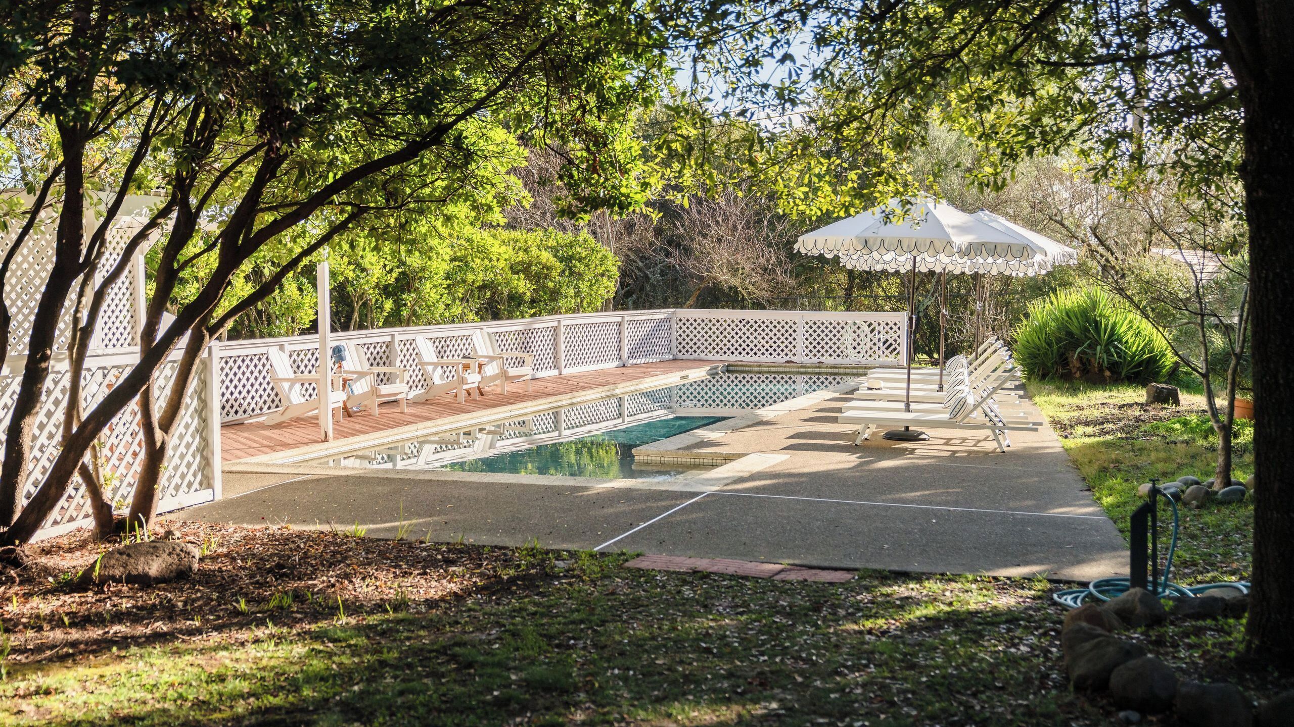 A pool area with a wooden deck, lounge chairs, and a white fence.