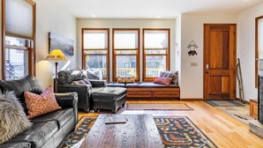 A living room with a leather sofa, a bench with cushions, a lamp, and large windows. - Pacific Street Townhome 514b by Avantstay Cute Townhouse in the Heart of Telluride! (Telluride)