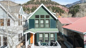 A two-story house with a green roof and multiple windows, surrounded by mountains and trees. - Pacific Street Townhome 514b by Avantstay Cute Townhouse in the Heart of Telluride! (Telluride)