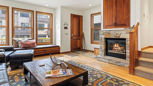 A spacious living room with a fireplace, large windows, a stone fireplace surround, and a cozy seating area. - Pacific Street Townhome 514b by Avantstay Cute Townhouse in the Heart of Telluride! (Telluride)