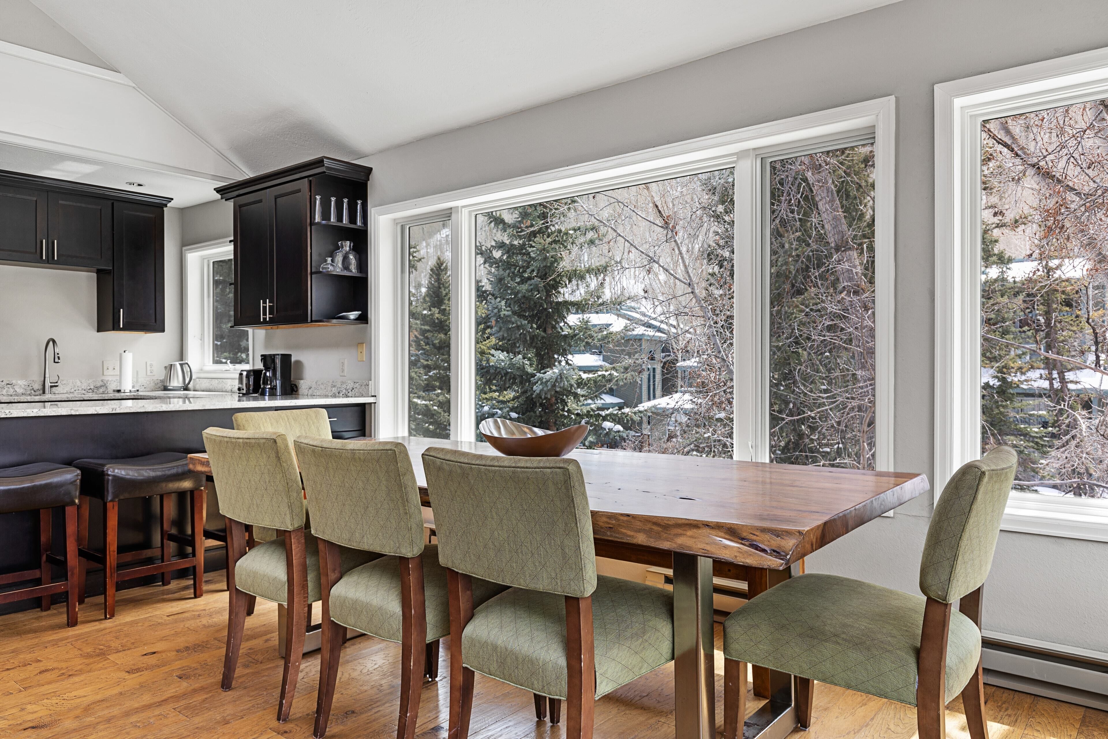 A modern kitchen with dark cabinetry, a wooden dining table, and green upholstered chairs.