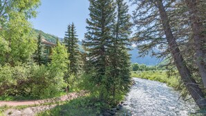 A river flowing through a forested area with a building in the background. - Ghostriders 10 by Avantstay Penthouse Suite w/ Large Patio & Mountain Views! (Telluride)
