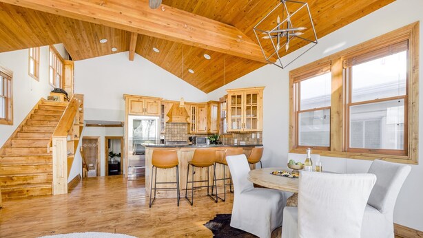 Uma cozinha ampla com armários de madeira, uma ilha central com banquetas e um espaço de jantar com mesa e cadeiras brancas.