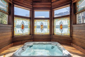 Una cabaña de madera con jacuzzi, ventanas amplias con vidrieras y vistas a las montañas.