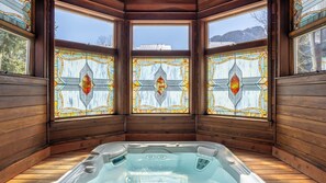 Una cabaña de madera con jacuzzi, ventanas amplias con vidrieras y vistas a las montañas.