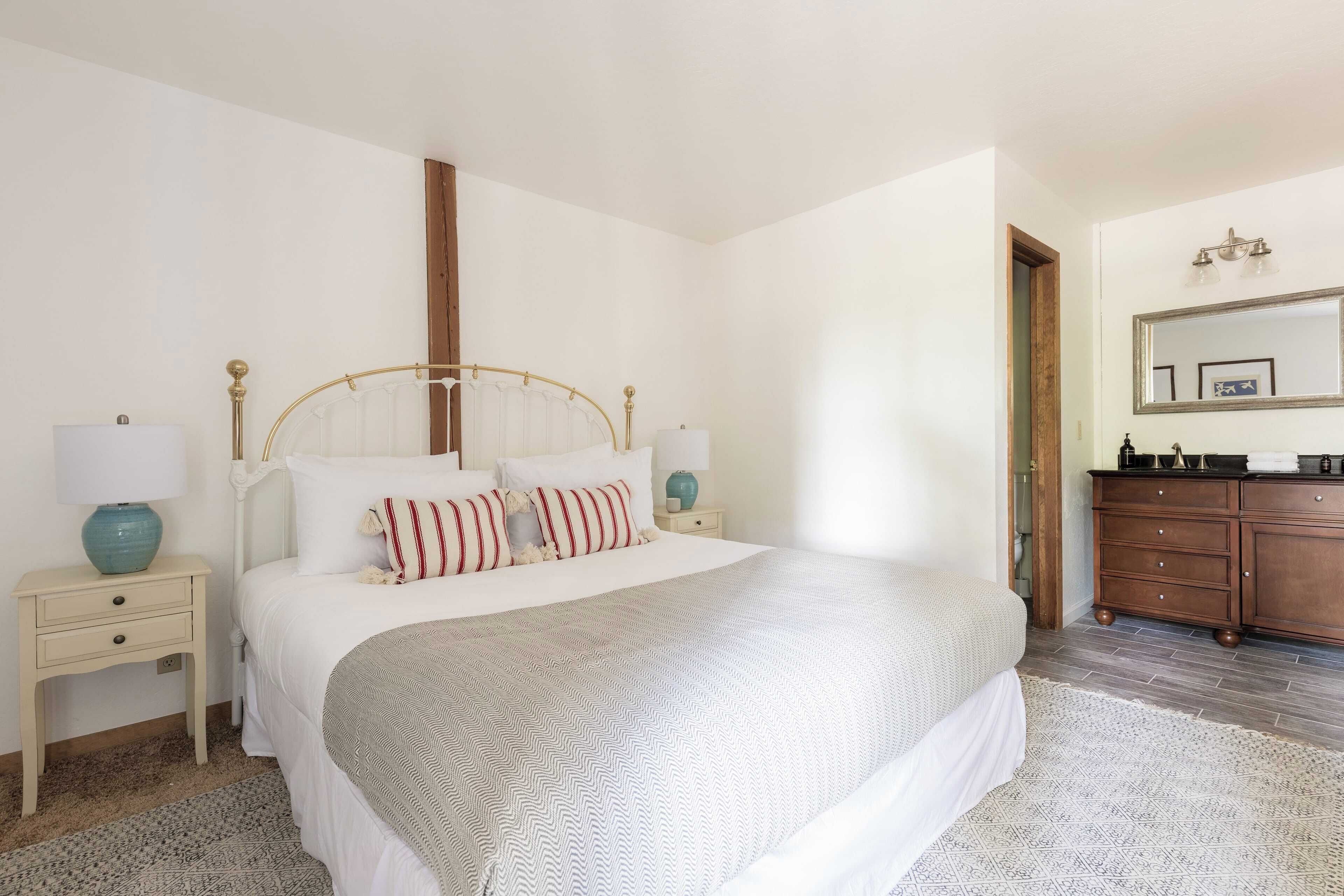A bedroom with a bed, bedside tables, a dresser, a mirror, and a patterned rug.