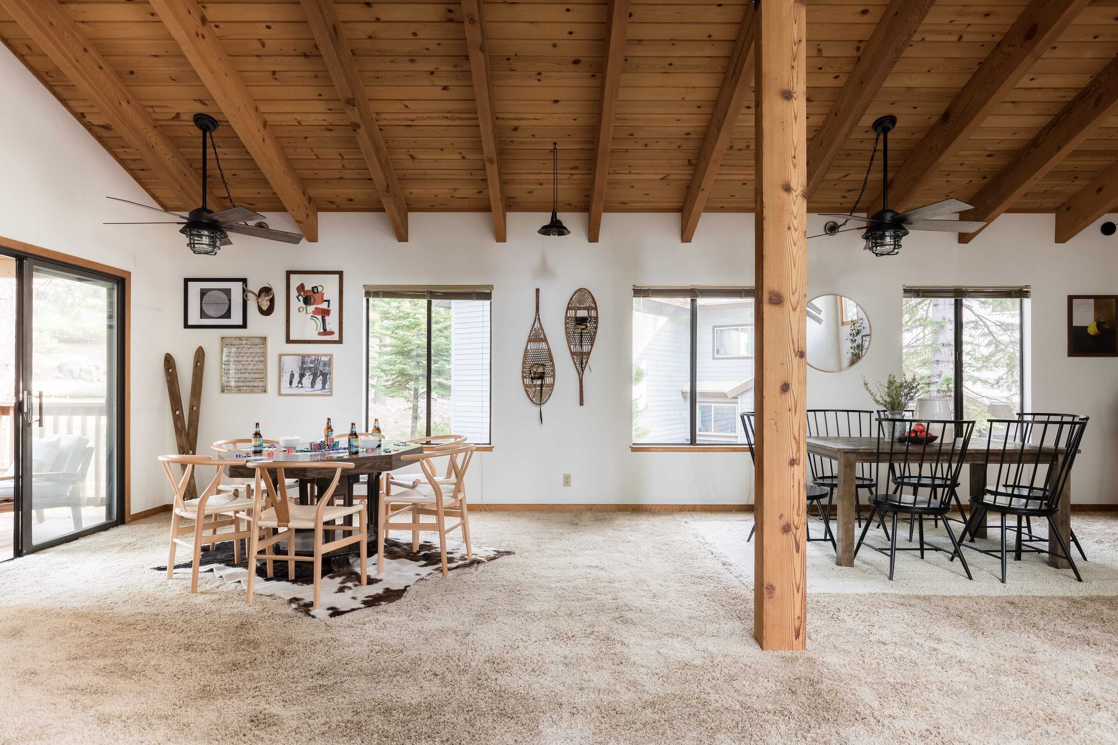 A spacious dining area with wooden ceiling beams, a large table with chairs, and a cowhide rug.