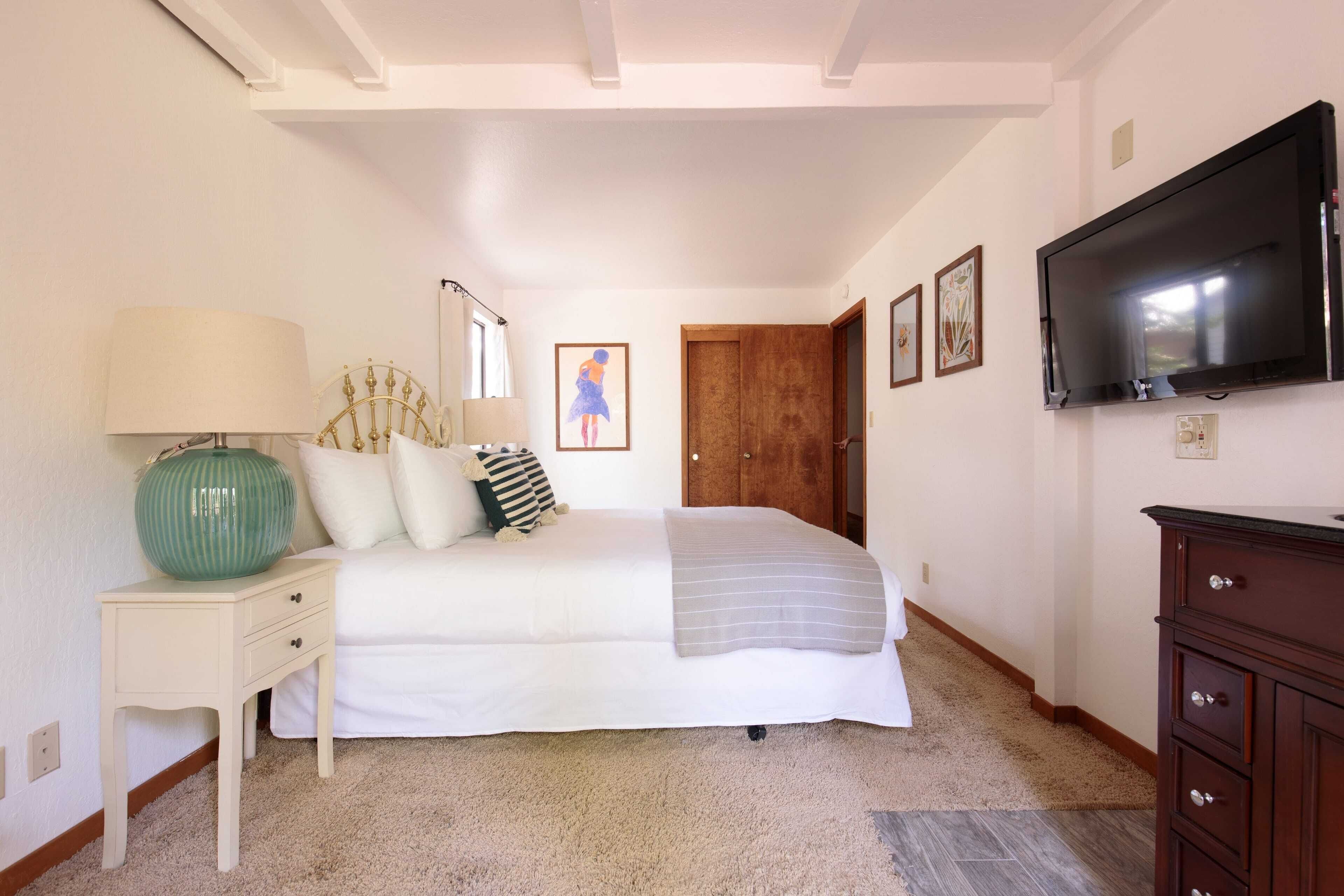 Une chambre à coucher avec un lit, une table de chevet, une commode, un téléviseur et une porte.