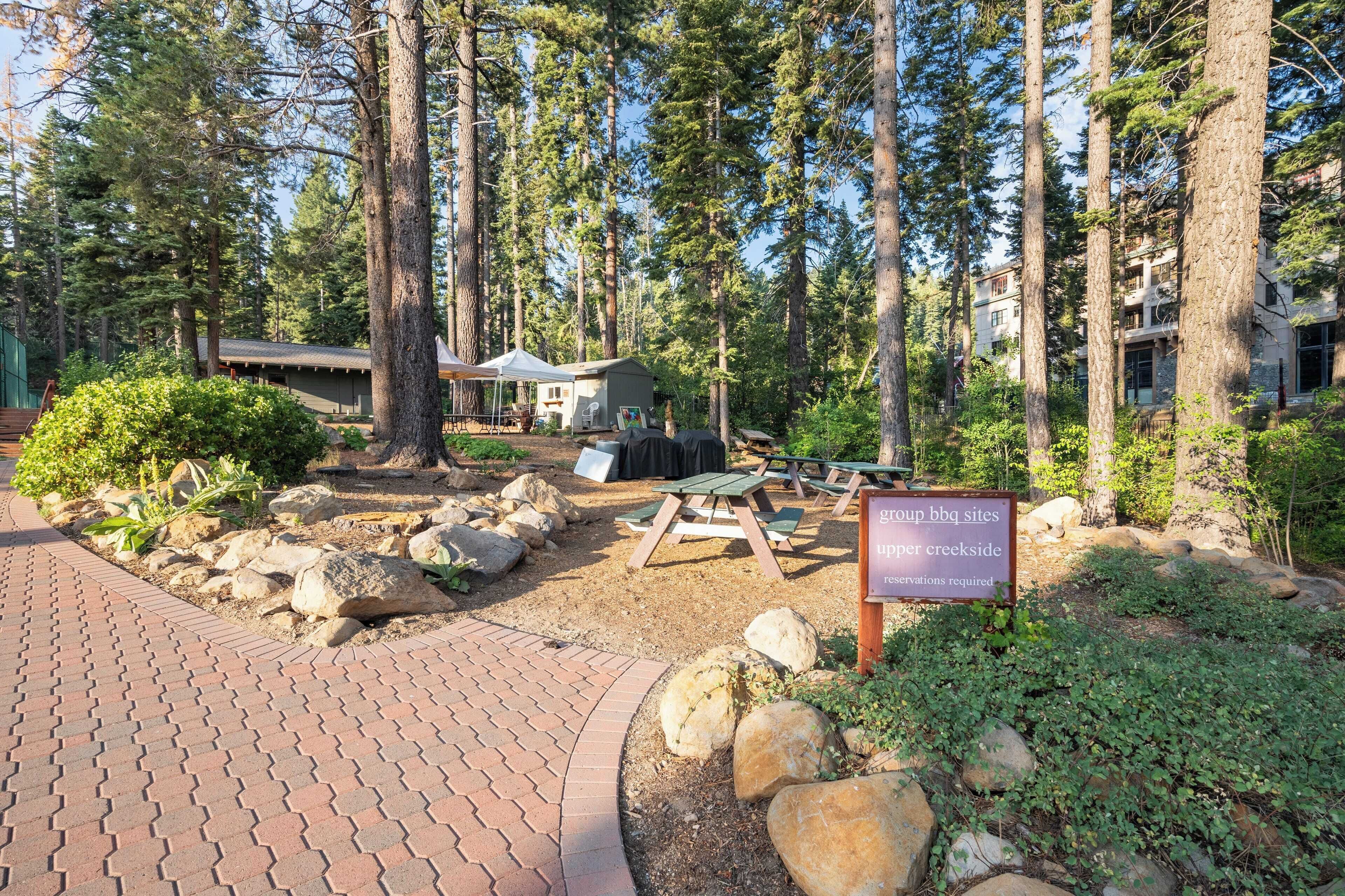 A campground with picnic tables, a barbecue area, and a sign indicating it is a public site with reservations required.