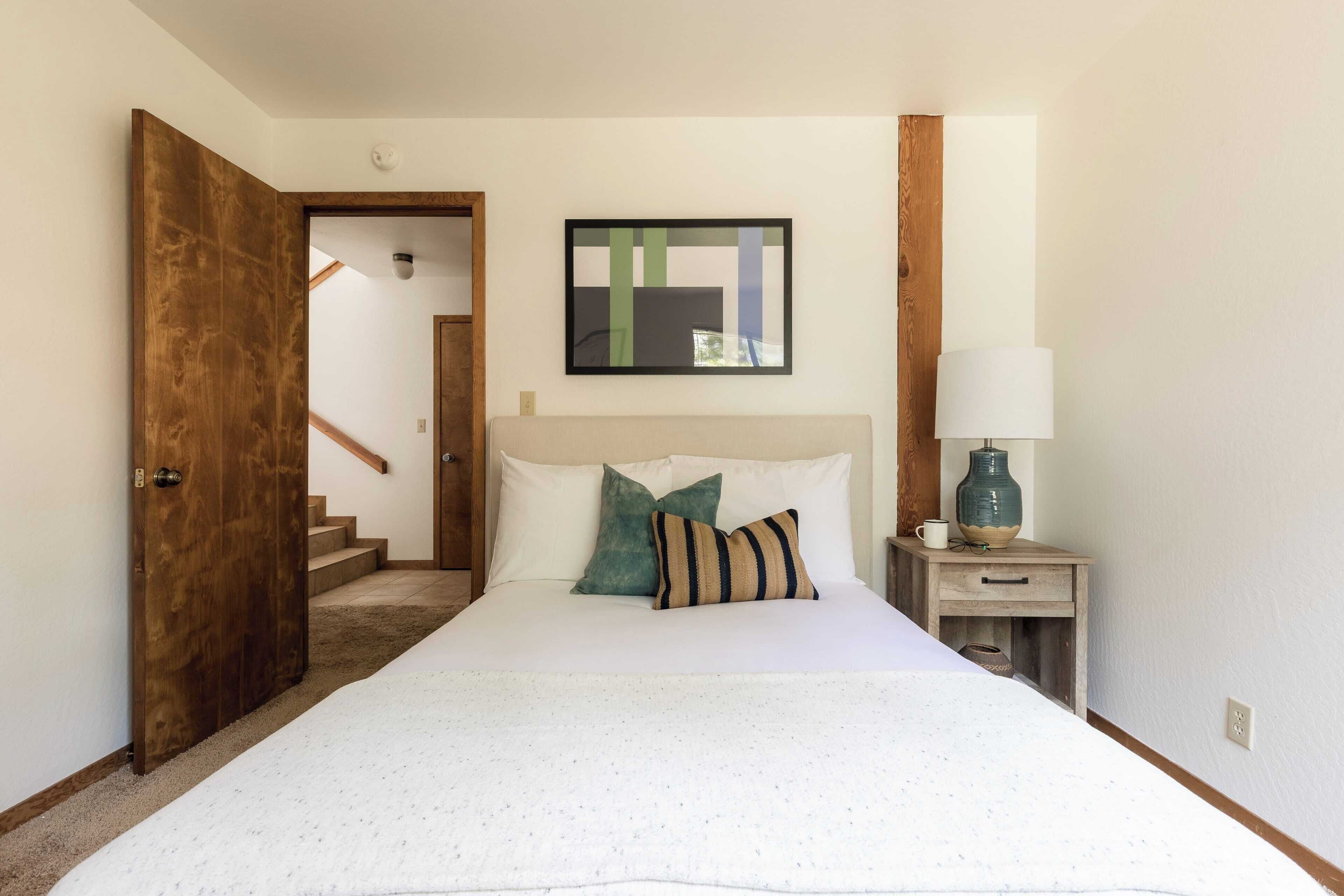 Een slaapkamer met een groot bed, een nachtkastje met een lamp, en een schilderij aan de muur.