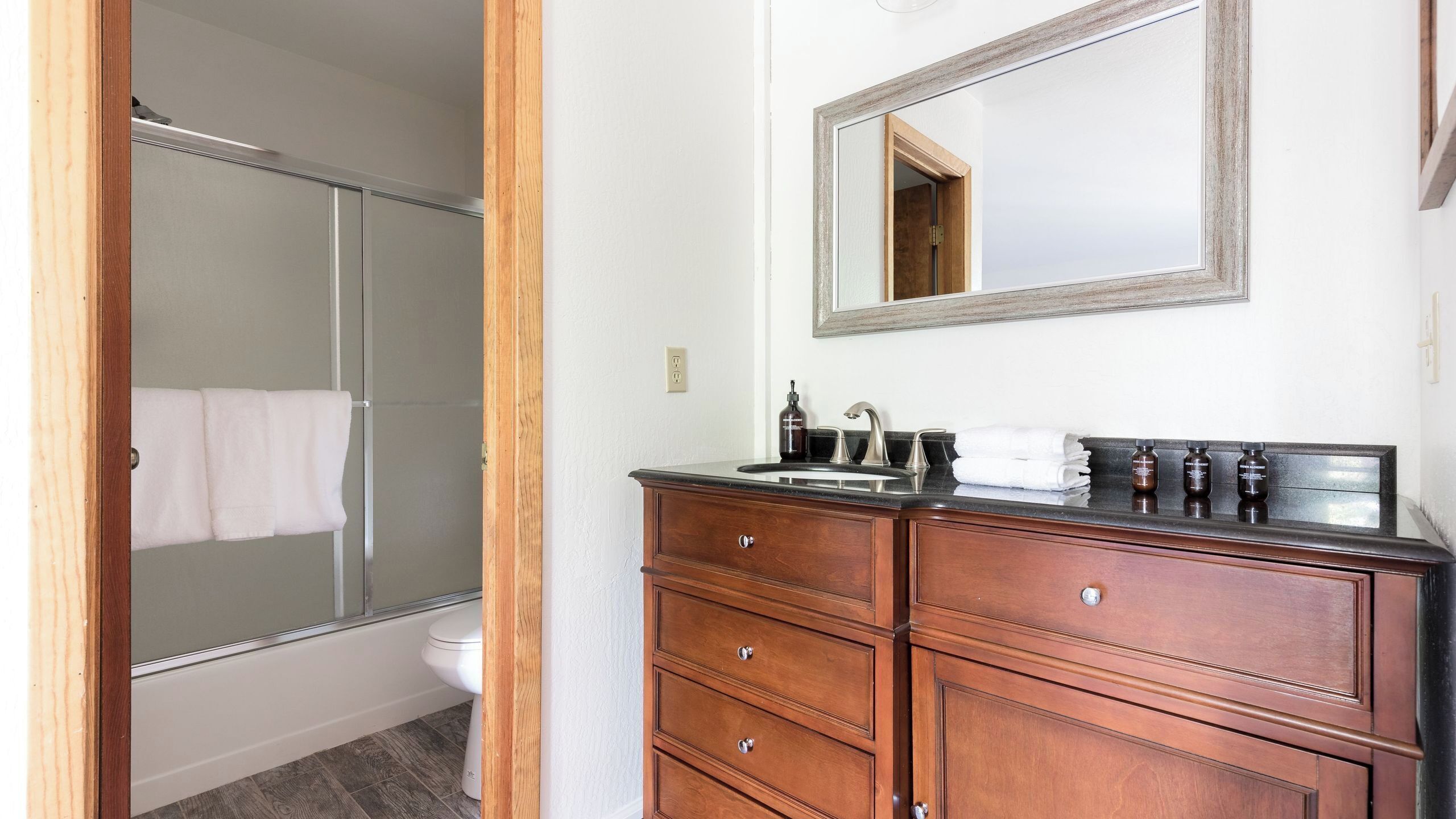 A bathroom with a shower, toilet, vanity with drawers, a mirror, and a sink with toiletries.