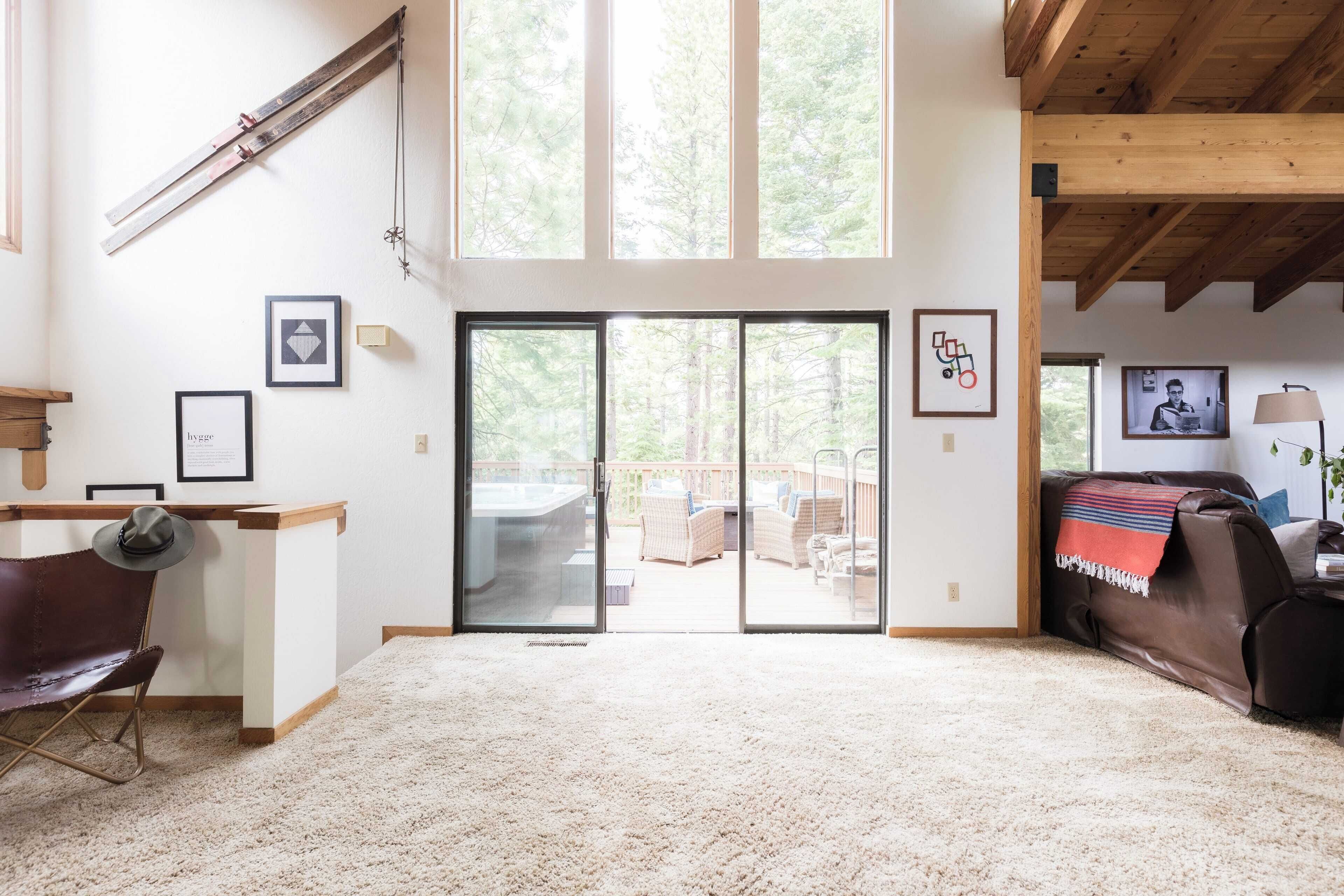 Un salón espacioso con un amplio ventanal corredera que da a un patio exterior, una zona de estar acogedora con un sofá y sillones, y un techo de madera.