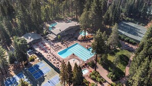 Vista aérea de um resort com várias piscinas, quadras de tênis e uma grande piscina central rodeada por áreas de descanso e árvores.