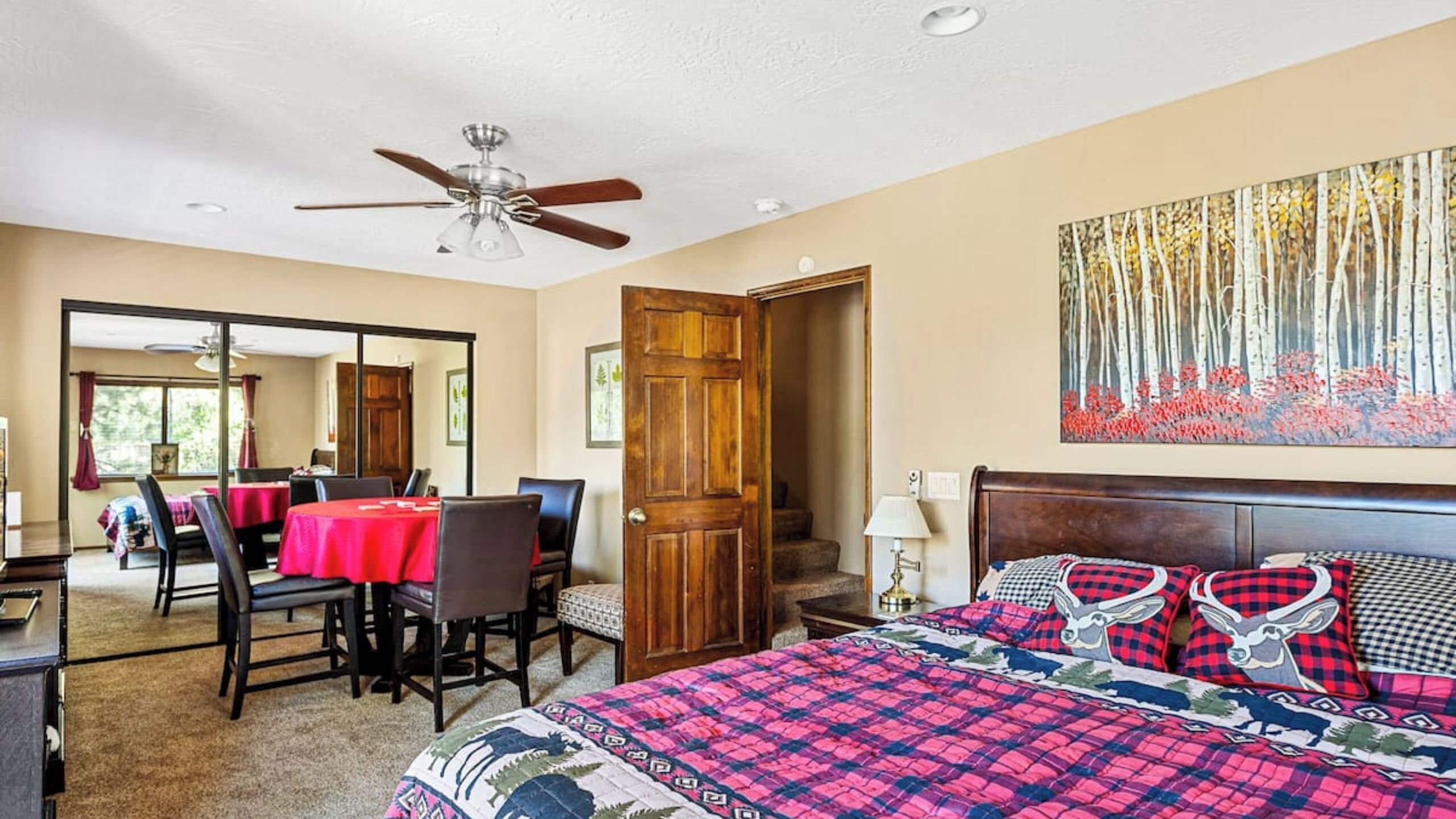 A bedroom with a bed, a desk, and a chair, a dining area with a table and chairs, and a hallway with a door.