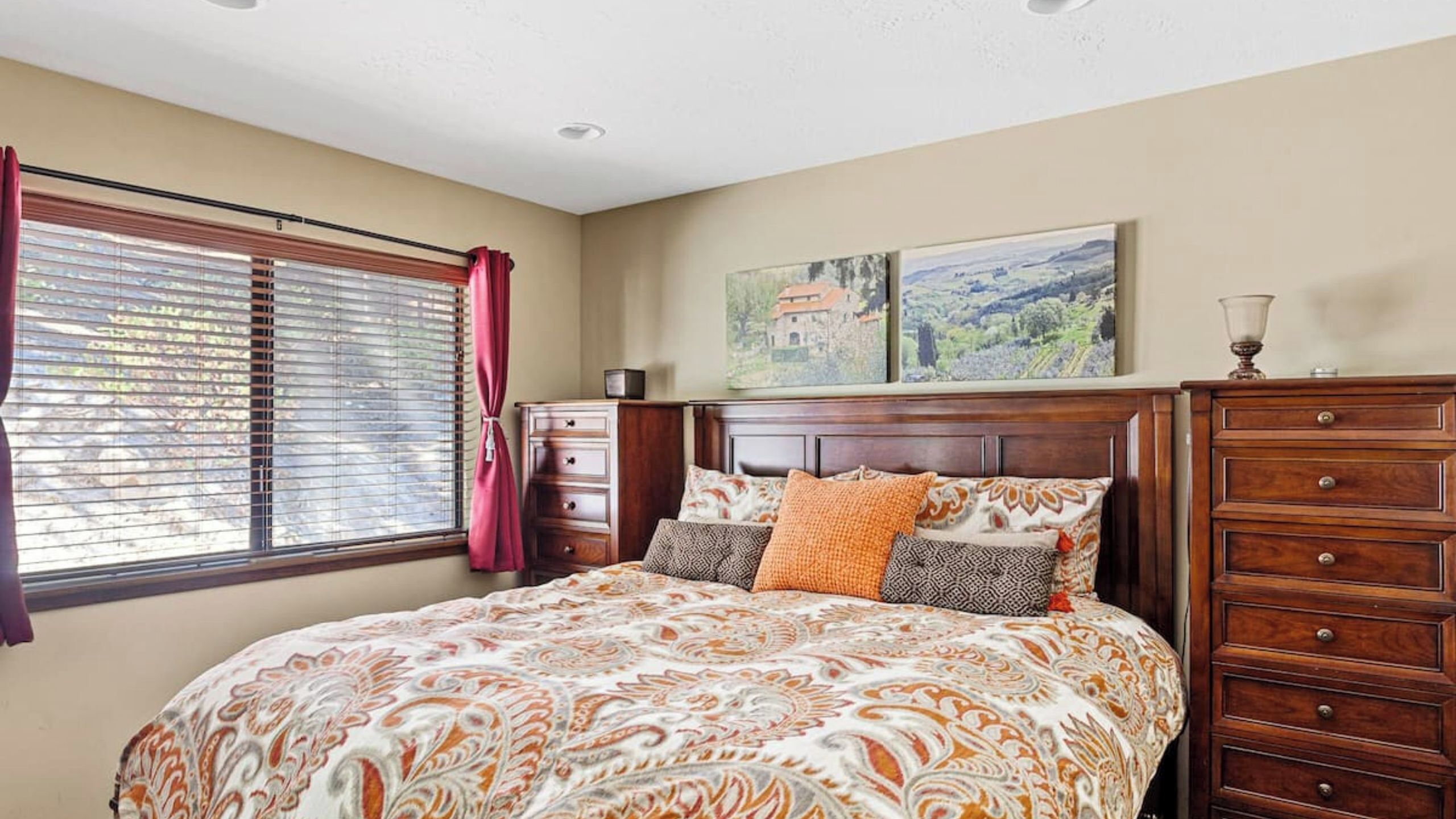 A bedroom with a large bed, a dresser, a nightstand, and a window with blinds.