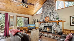 A cozy living room with a stone fireplace, wooden ceiling, and a television. - Beautifully Remodeled Kitchen Peaceful Mountain Views Sutter by Avantstay (Lake Arrowhead)
