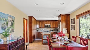 A spacious kitchen with wooden cabinets, a central island, and a dining area with red chairs. - Beautifully Remodeled Kitchen Peaceful Mountain Views Sutter by Avantstay (Lake Arrowhead)