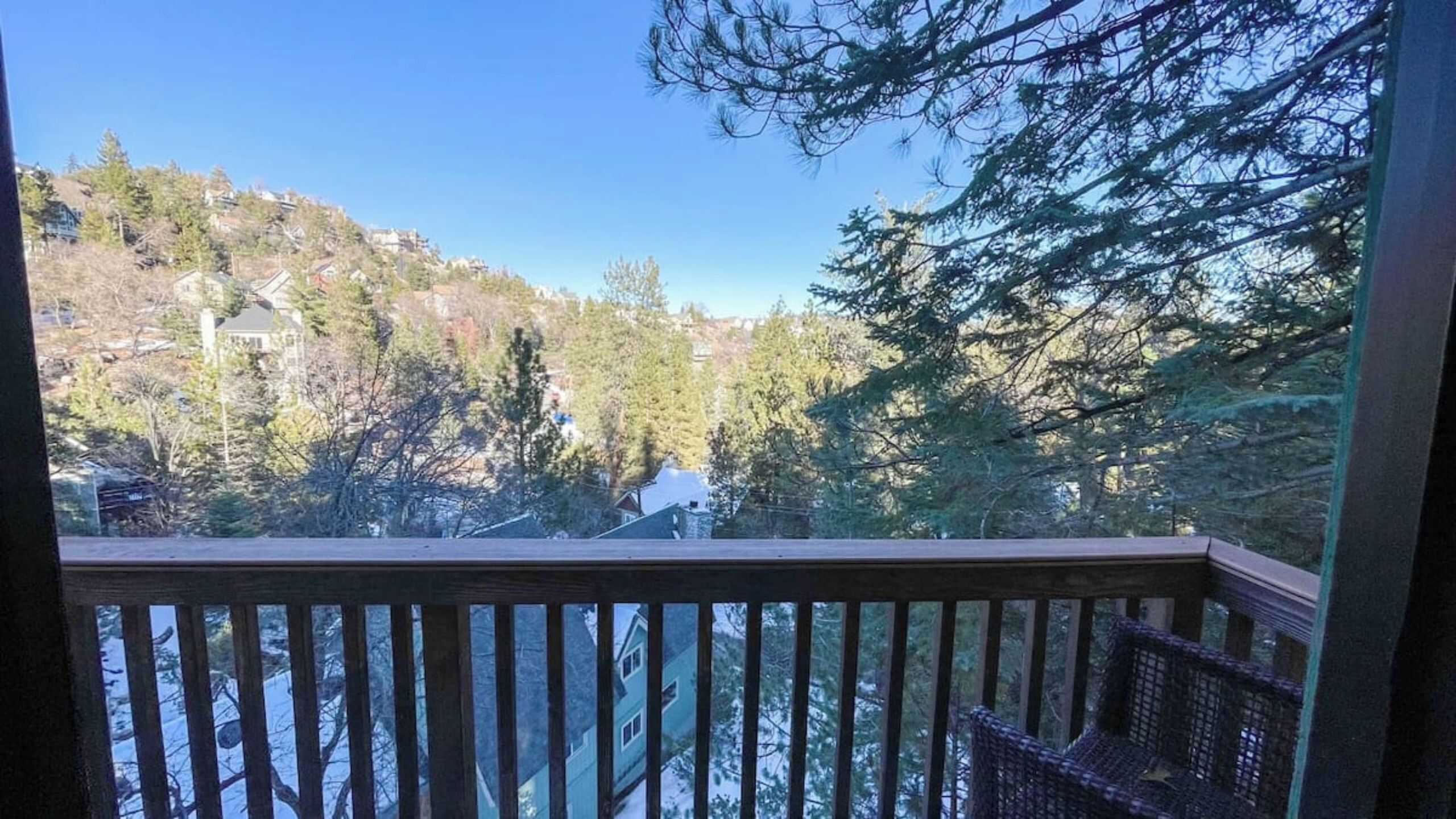 A view from a balcony with a wooden railing, overlooking a residential area with houses and trees.