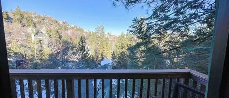 A view from a balcony with a wooden railing, overlooking a residential area with houses and trees.