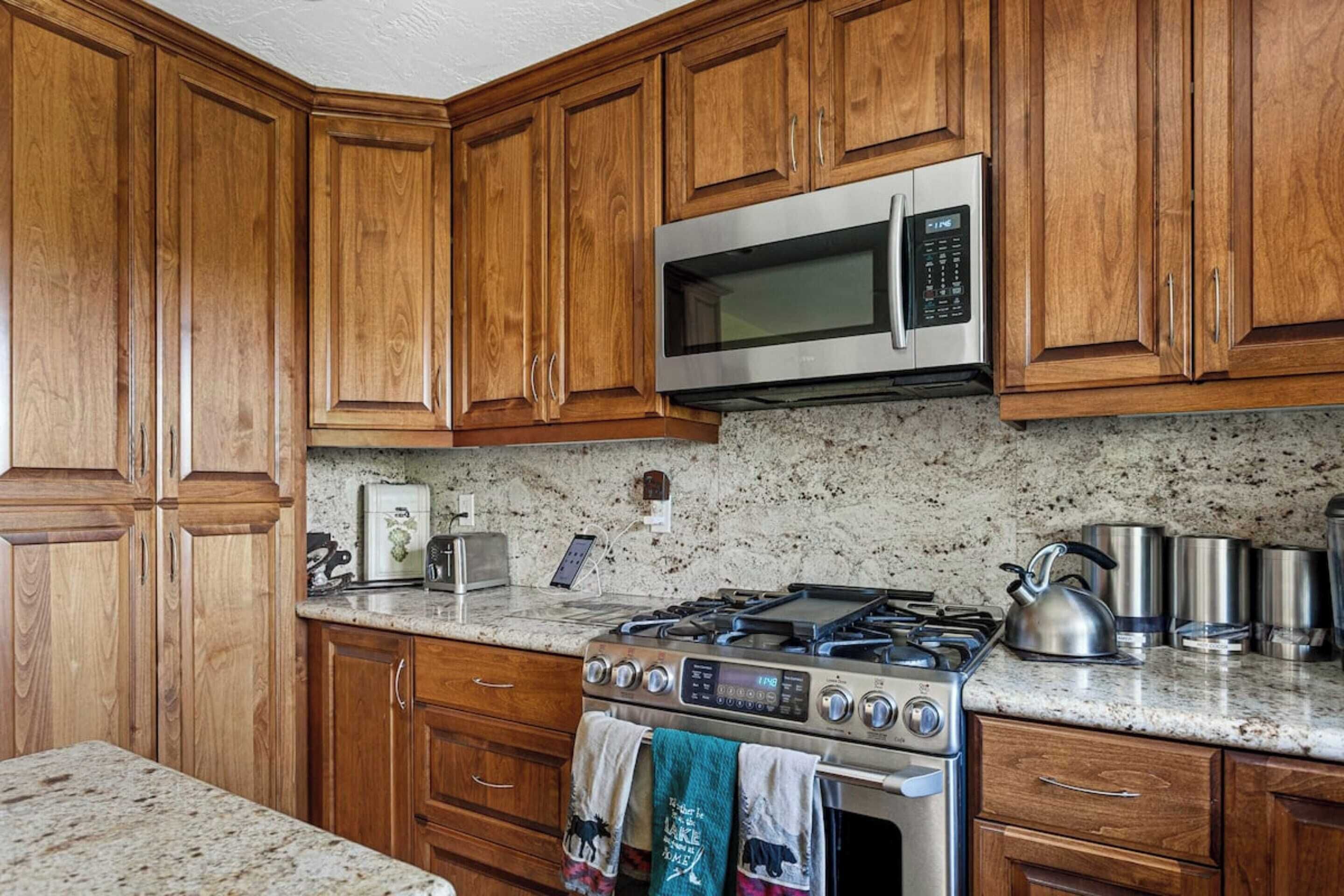 A kitchen with wooden cabinets, a stainless steel microwave, a gas stove, and granite countertops.