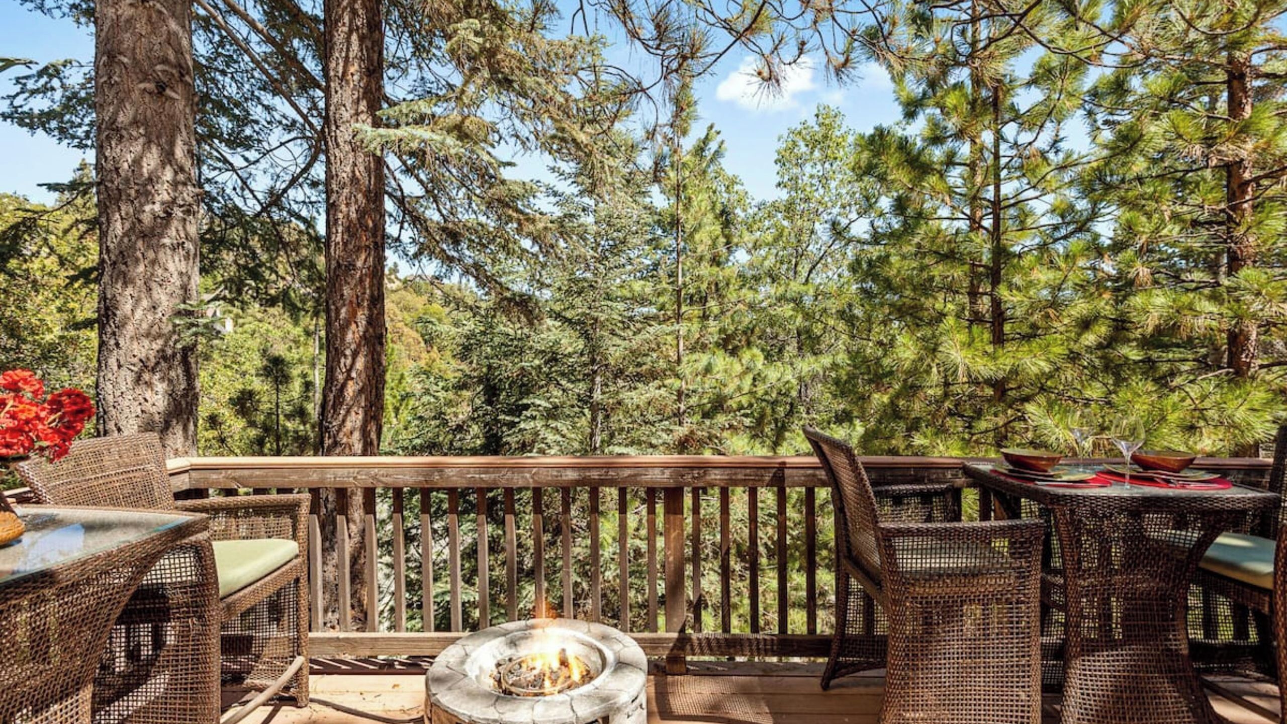 An outdoor deck with wicker furniture, a fire pit, and a view of a forest.
