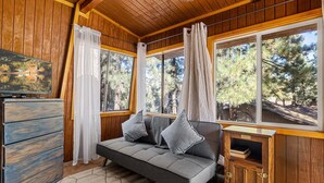 Ein gemütliches Blockhaus-Interieur mit einer Couch, Holzwänden, großen Fenstern und einem Fernseher.