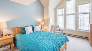 A bedroom with a large bed, two bedside tables with lamps, a chair, and a dresser. There are three windows providing natural light. - Etta Place Too 113 by Avantstay Close to Town & The Slopes! In Complex w/ Communal Pool & Hot Tub (Telluride)