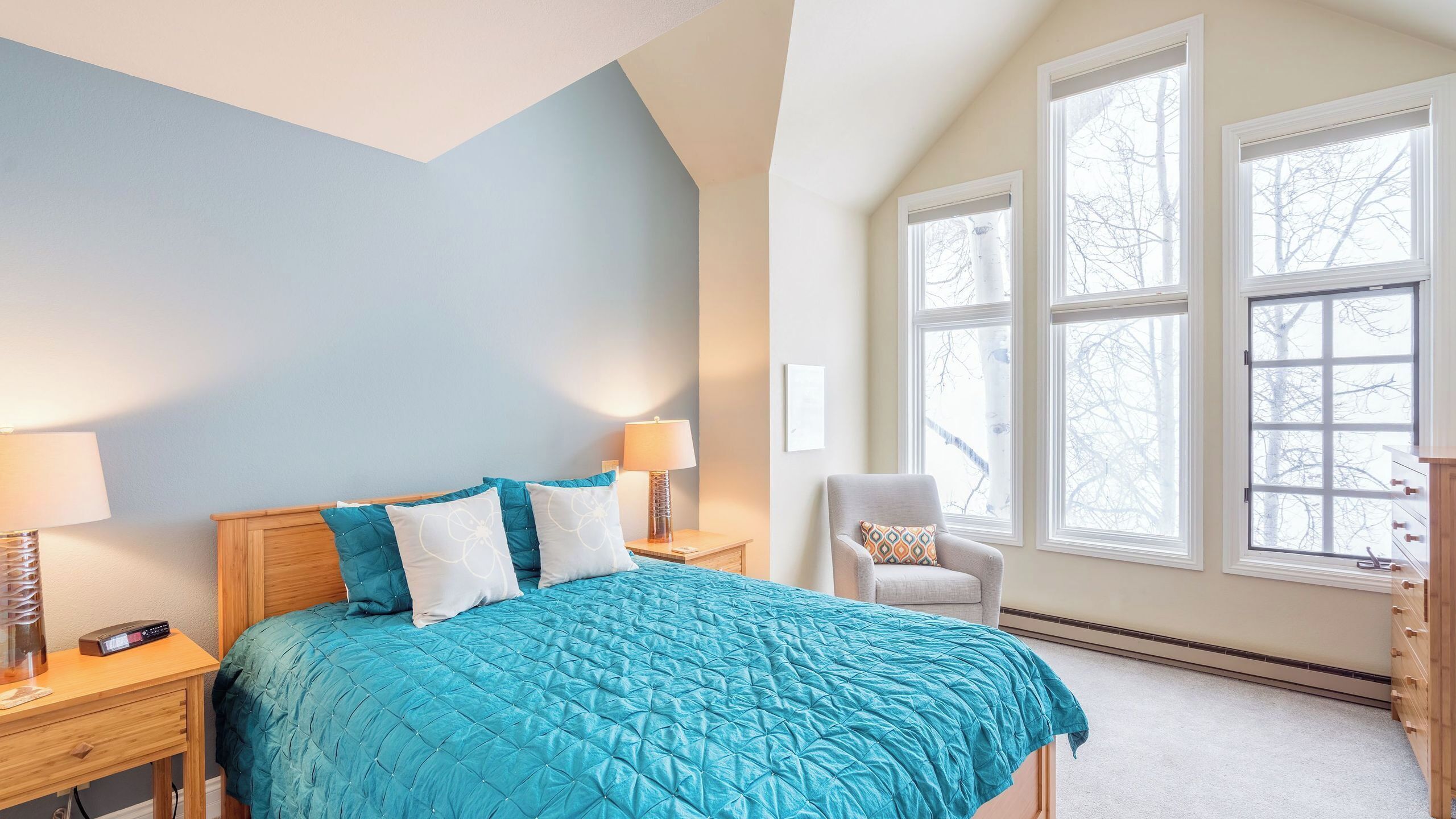 A bedroom with a bed, nightstands, a chair, and large windows.