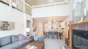 A spacious living room with a grey sofa, a wooden coffee table, and a fireplace. A staircase leads to an upper level. - Etta Place Too 113 by Avantstay Close to Town & The Slopes! In Complex w/ Communal Pool & Hot Tub (Telluride)
