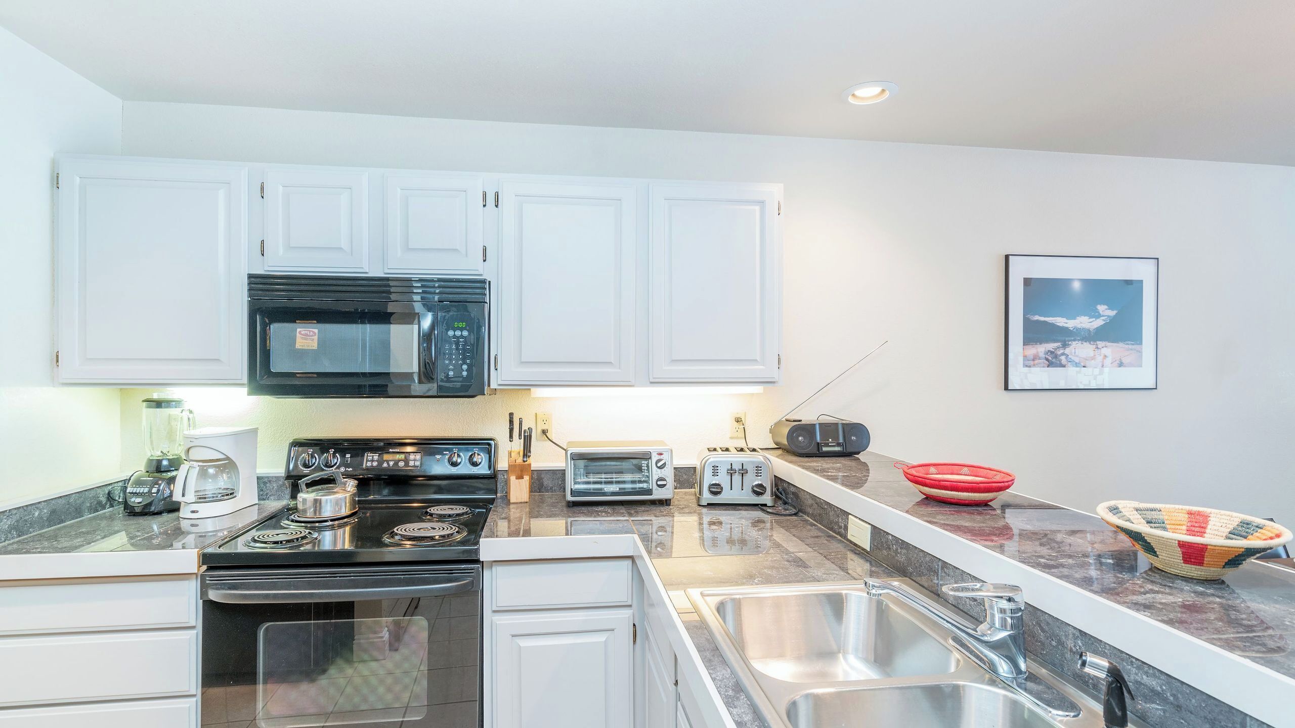 A modern kitchen with white cabinets, a microwave, a stove, a toaster, and a sink.