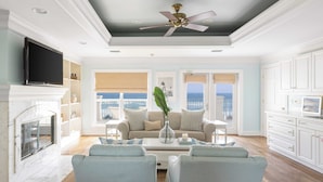 A living room with a fireplace, a television, and a view of the ocean. - Promenade by Avantstay Beach Front Mansion w/ Breathtaking Views & Pool! (Miramar Beach)