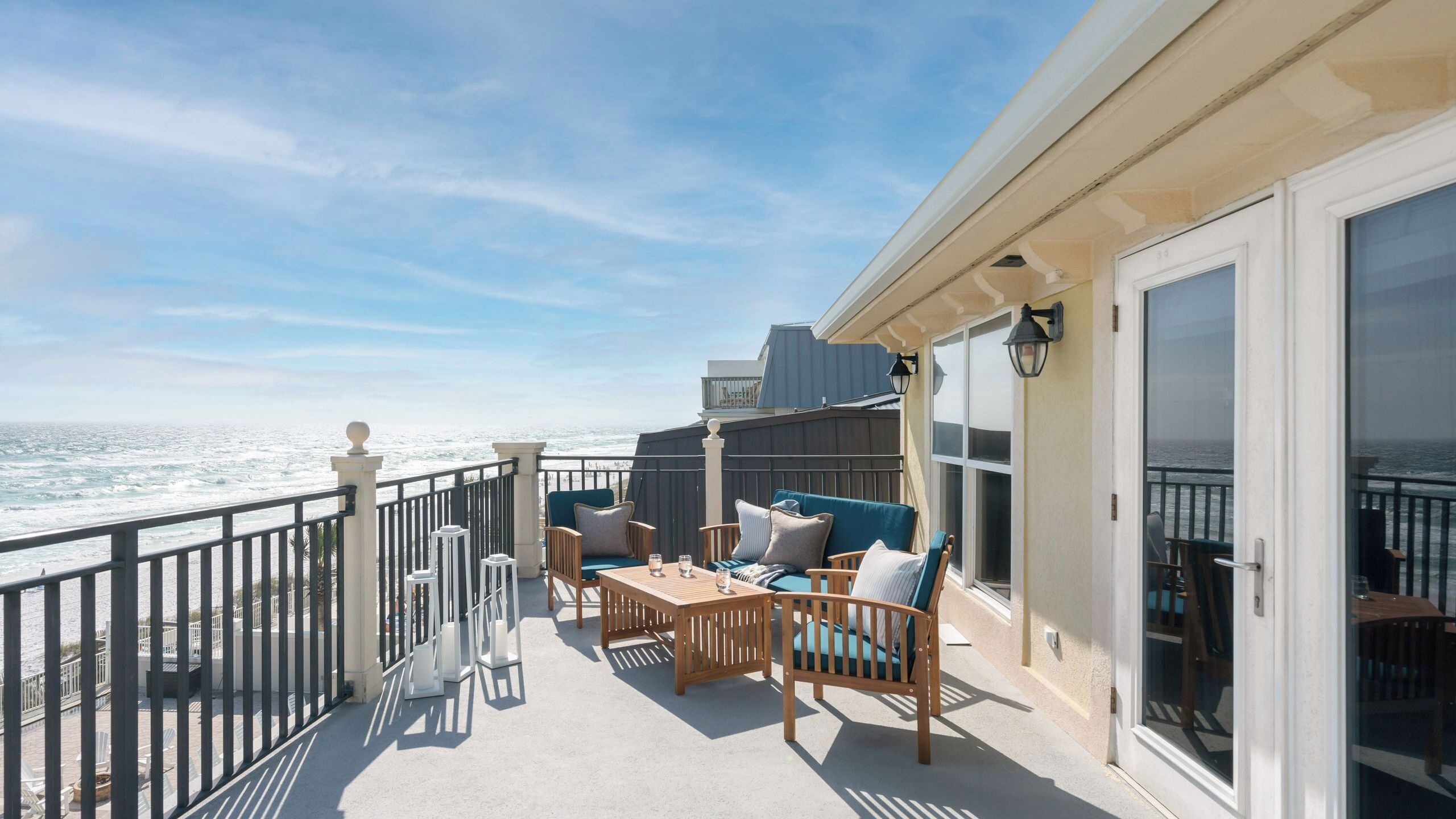 A balcony with a view of the ocean, furnished with a table and chairs, and a sliding glass door leading to an interior space.