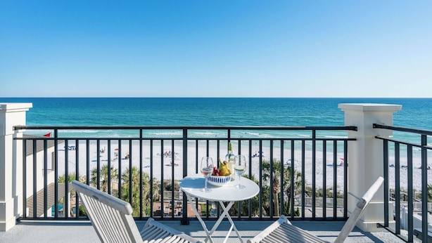 A balcony with a table set for two, overlooking a beach with people and umbrellas. - Promenade by Avantstay Beach Front Mansion w/ Breathtaking Views & Pool! (Miramar Beach)