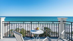 A balcony with a table set for two, overlooking a beach with people and umbrellas.