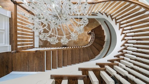 A spiral staircase with wooden steps and white balusters, leading to a room with a large chandelier. - Promenade by Avantstay Beach Front Mansion w/ Breathtaking Views & Pool! (Miramar Beach)
