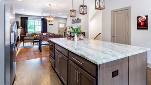 A modern kitchen with a marble countertop, wooden cabinets, pendant lighting, and a coffee-themed wall decoration. - Waverly by Avantstay Nashville-inspired Townhome w/ Luxury Kitchen, Pool Table (Nashville)