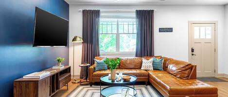 A living room with a sectional sofa, a flat-screen TV mounted on the wall, a ceiling fan, and a sign reading "Nashville".