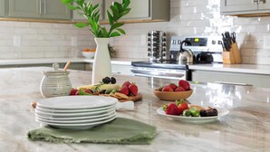 A kitchen with a marble countertop, a white vase with green leaves, a kettle, and various fruits and pastries. - Waverly by Avantstay Nashville-inspired Townhome w/ Luxury Kitchen, Pool Table (Nashville)