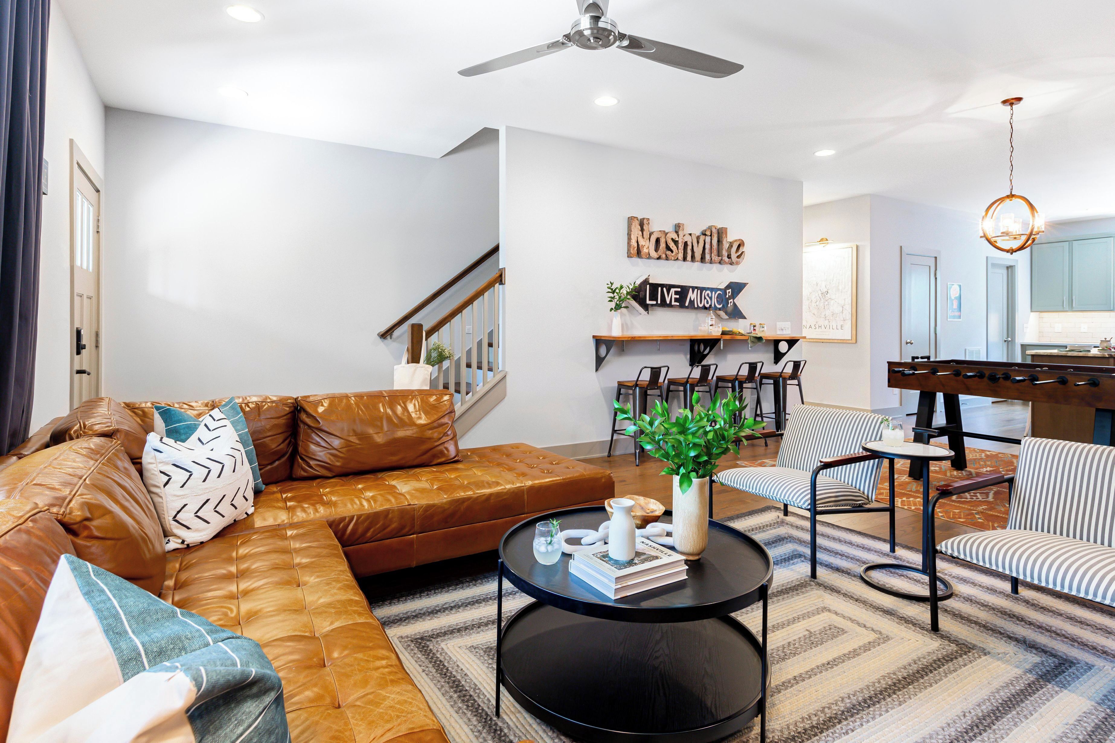 A modern living room with a leather sofa, a coffee table, striped chairs, and a wall-mounted shelf with decorative items.