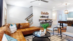 A modern living room with a leather sofa, a coffee table, striped chairs, and a wall-mounted shelf with decorative items. - Waverly by Avantstay Nashville-inspired Townhome w/ Luxury Kitchen, Pool Table (Nashville)