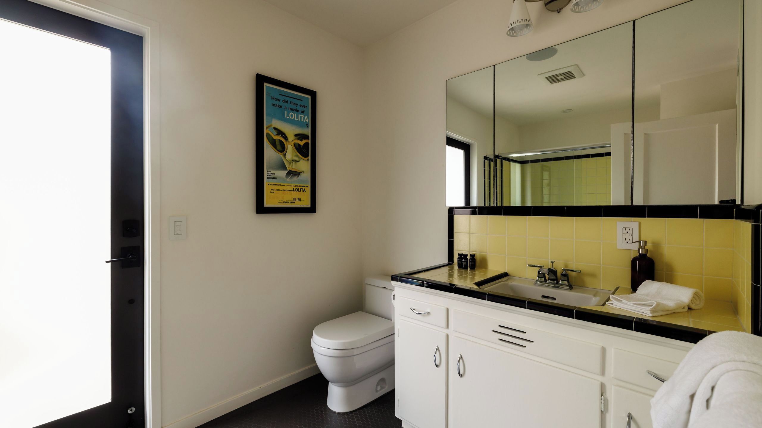 Un baño con inodoro, lavabo, espejo y un cartel en la pared.