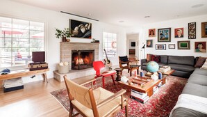 A living room with a fireplace, a sofa, a red chair, a wooden coffee table, and a bookshelf. - Marquee By Avantstay Modern Stylish Estate w/ Pool & Entertainers Courtyard (Sonoma)