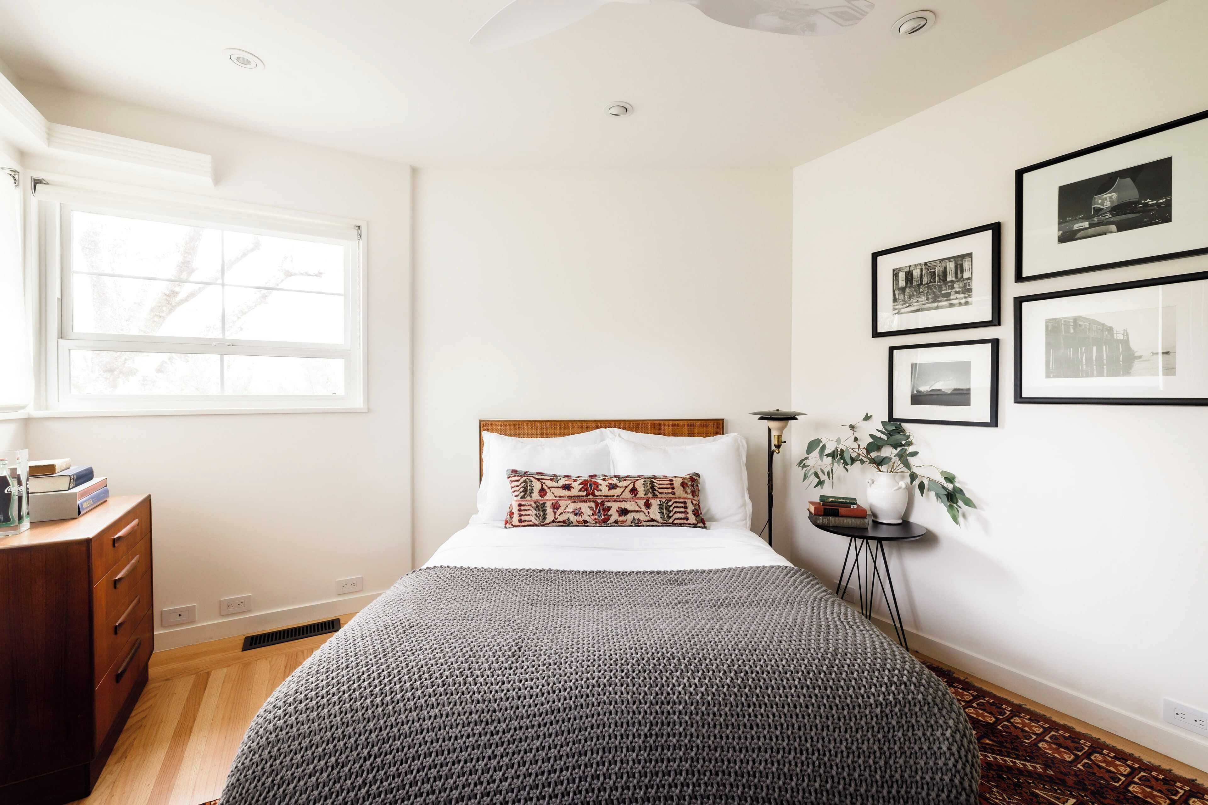 Un dormitorio con cama, cómoda, ventana y cuadros en la pared.